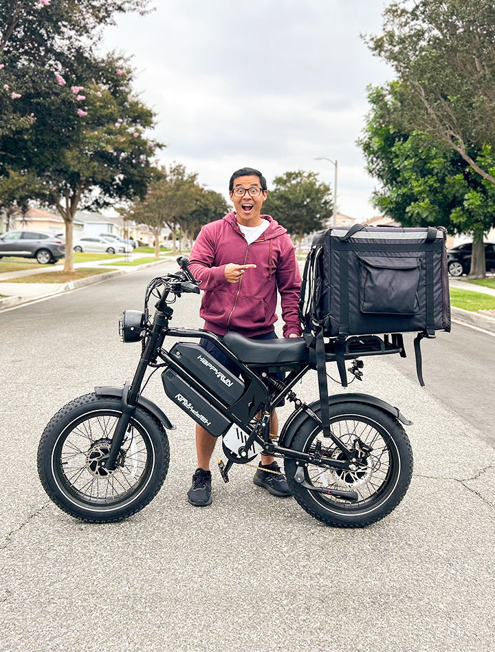 Man standing with HappyRun G70 750W fat-tire electric cargo bike in matte black color, Adult e-bike featuring a dual battery setup, powerful dual-motor system, aluminum alloy cargo-ready frame, front suspension fork, padded rear cargo seat with backrest, integrated rear cargo rack, hydraulic disc brakes, front LED headlight, and backlit LCD display, Class 3 electric bike built for hauling gear and long-range rides. Similar to Macfox Electric Bicycle 48V 500w E-Bike - X7, KETELES Electric Bike for Adult.