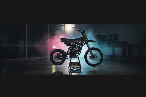A black electric dirt bike with knobby tires is displayed on a black stand in a dark studio setting with dramatic pink and blue smoke and a bright light in the background. The stand features the brand name 'HAPPYRUN FORCED'.
